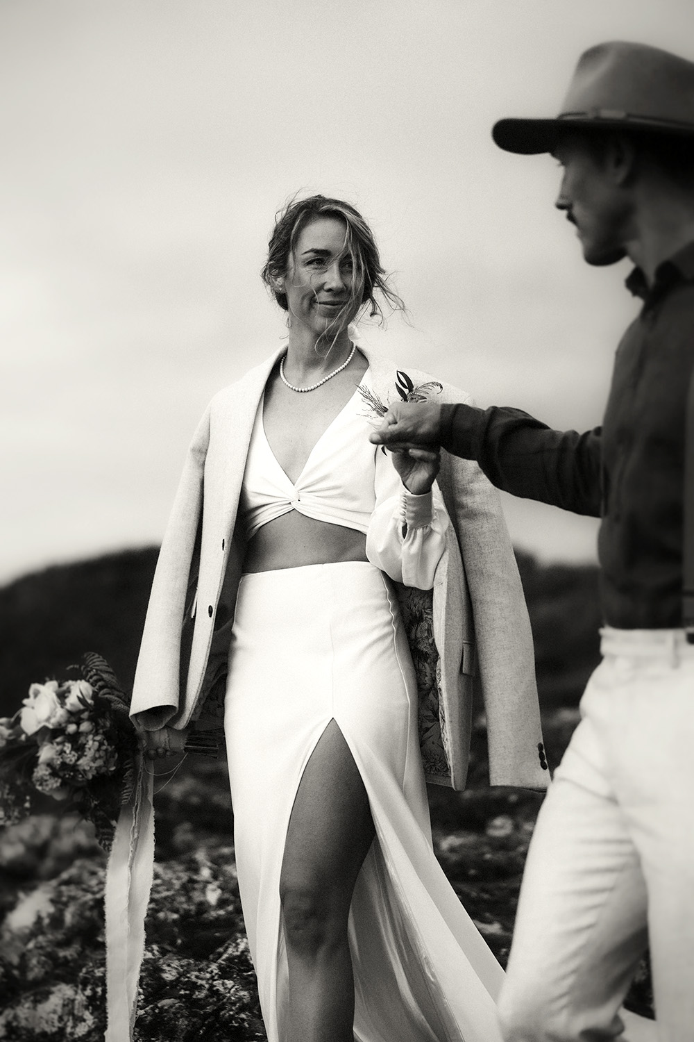 Bride in modern white dress holding hands with groom outdoors