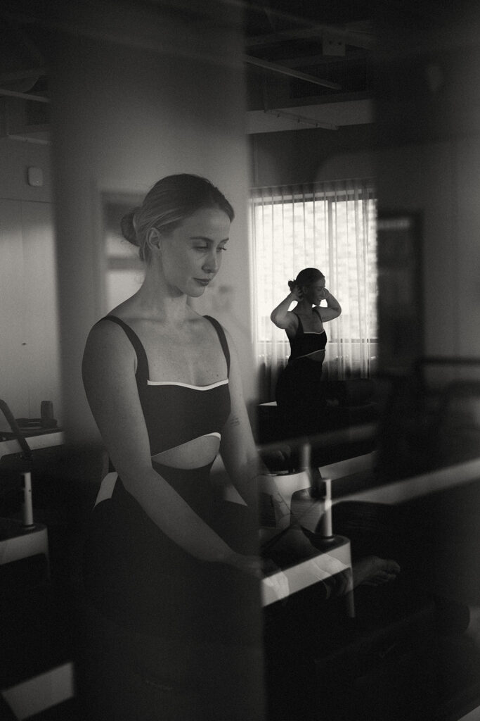 Black-and-white image of a woman in a Pilates studio, captured through a reflection with a calm, focused expression, by a Sunshine Coast brand and movement photographer.