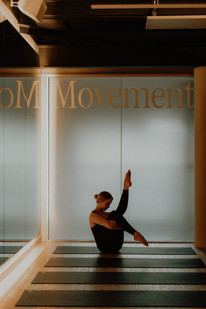 Woman in a black outfit balancing in a Pilates pose on a yoga mat inside a minimalist movement studio, photographed by a Sunshine Coast brand photographer.