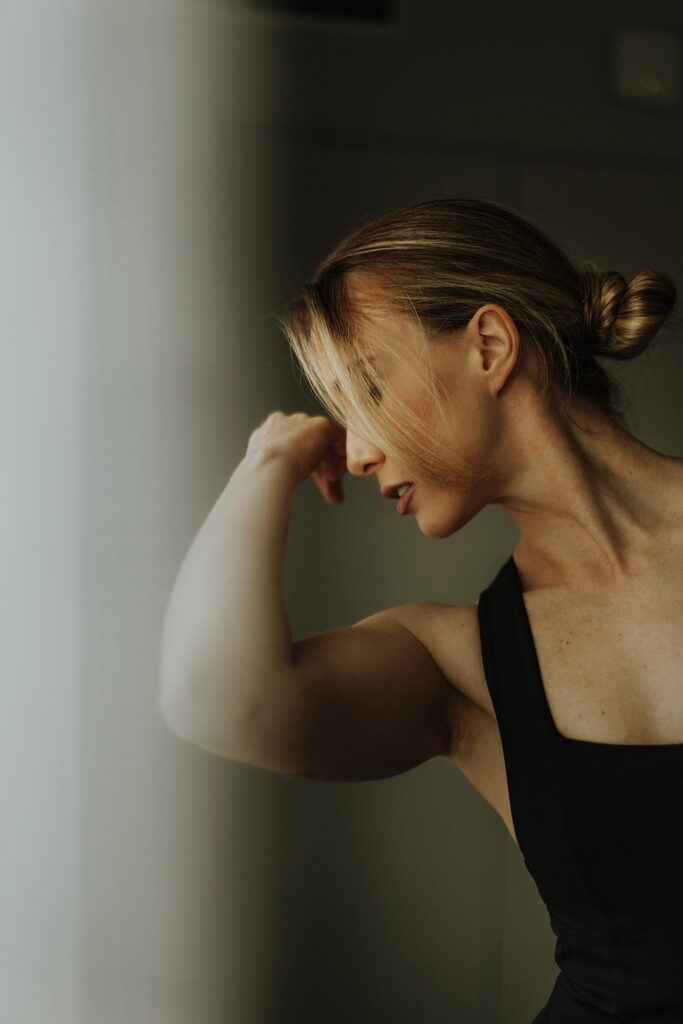 Close-up of a woman in a black top flexing her arm near a softly lit wall, captured by Sunshine Coast brand photographer Nicci K.