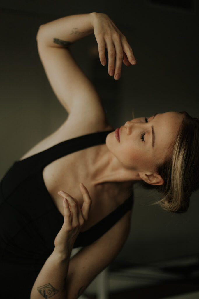 Close-up of a woman in a black outfit with eyes closed, arms curved gracefully in a dance-inspired pose, captured by Sunshine Coast brand and movement photographer.