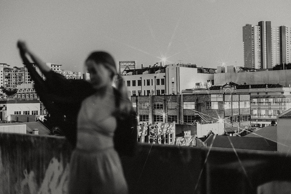 Blurred silhouette of a woman in motion on a rooftop at sunset with a clear city skyline in the background, captured by Sunshine Coast brand photographer.