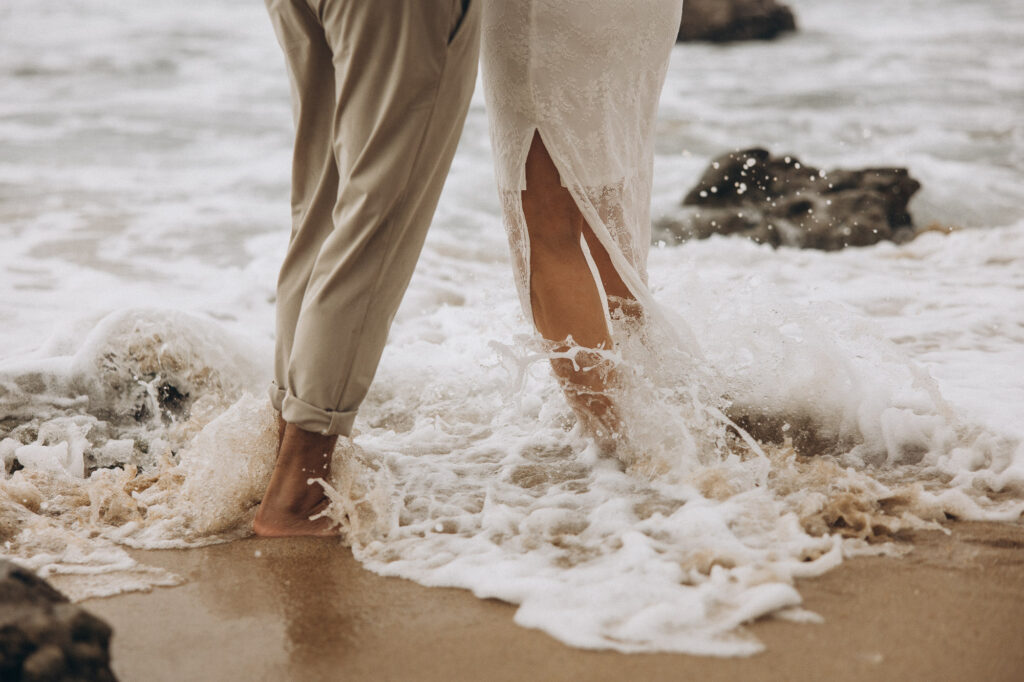 Bride and groom barefoot in the ocean waves during Coolum Beach elopement, Sunshine Coast wedding photography capturing adventurous coastal love story
