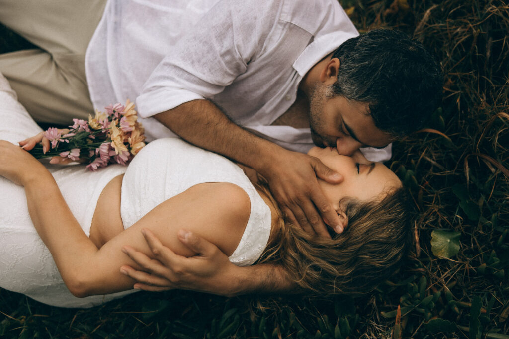 Romantic Sunshine Coast elopement photography, bride holding bouquet while groom kisses her gently in coastal grass at Coolum Beach