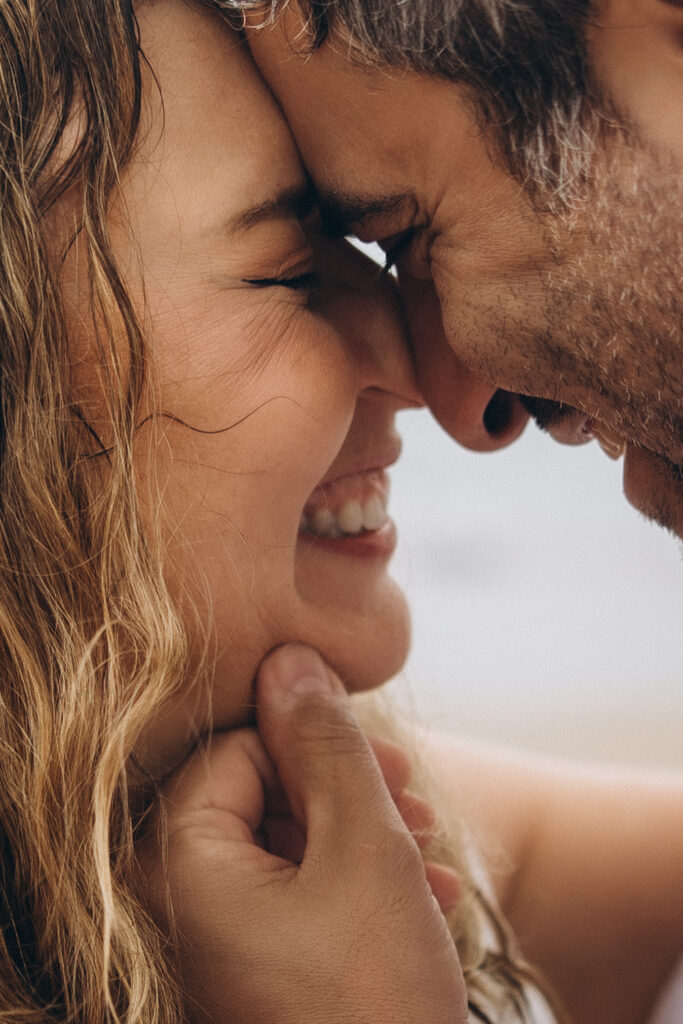 Bride kisses groom on cheek at beach elopement portrait, Sunshine Coast couples photographer capturing candid love and raw emotion under rain umbrella”