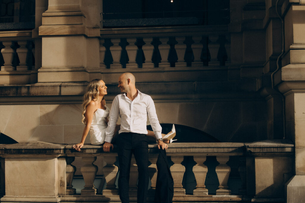 Golden-hour elopement photo at Treasury Brisbane featuring a bride and groom sharing laughter on the sandstone balcony. A cinematic and romantic city moment captured by Nicci K Photography, Brisbane elopement and wedding photographer creating modern, emotive love stories.