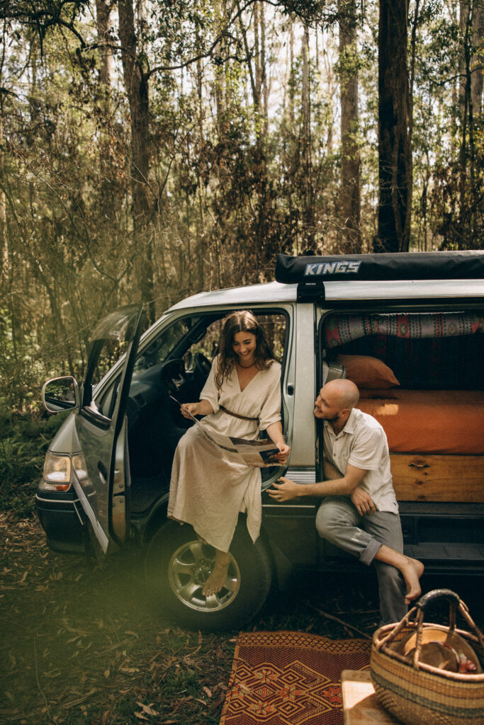 Cinematic couples storytelling session in the Sunshine Coast Hinterland, featuring a barefoot couple planning their adventure with a map beside their camper van in the Maleny and Mapleton forests. Captured by Sunshine Coast photographer Nicci K, this van-life inspired shoot highlights authentic, documentary-style moments and emotive connection in nature.