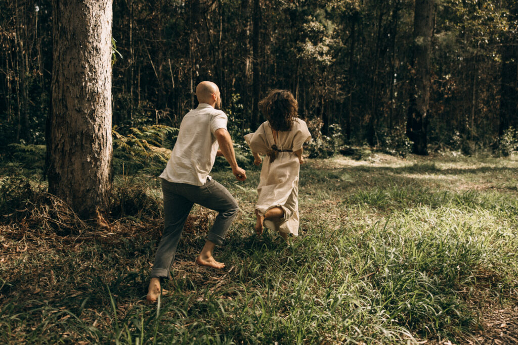 Playful barefoot couple running through the Mapleton rainforest during a cinematic Sunshine Coast Hinterland storytelling session. A romantic, nature-inspired couples photoshoot capturing motion, connection and adventure in the forest.