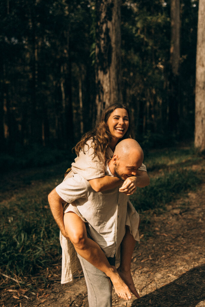 Cinematic Sunshine Coast forest couples photography at golden hour, capturing a warm, documentary-style moment of a couple smiling and holding each other during their storytelling session.