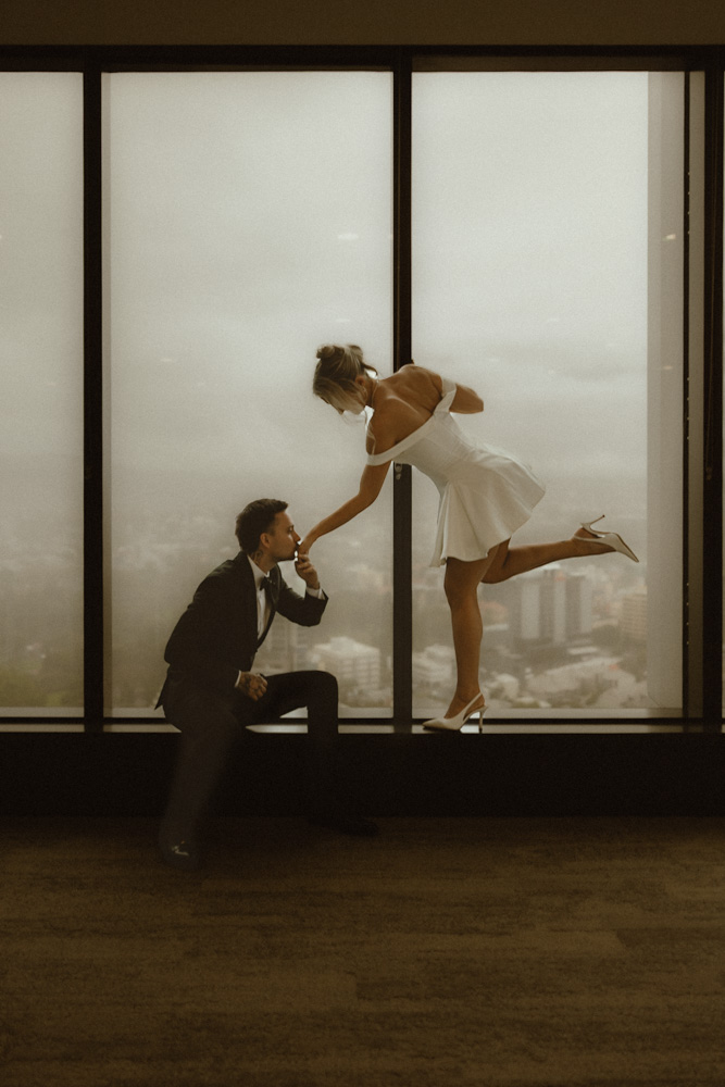 Groom dipping bride for a kiss in front of floor-to-ceiling windows overlooking the Brisbane skyline at the Registry Office