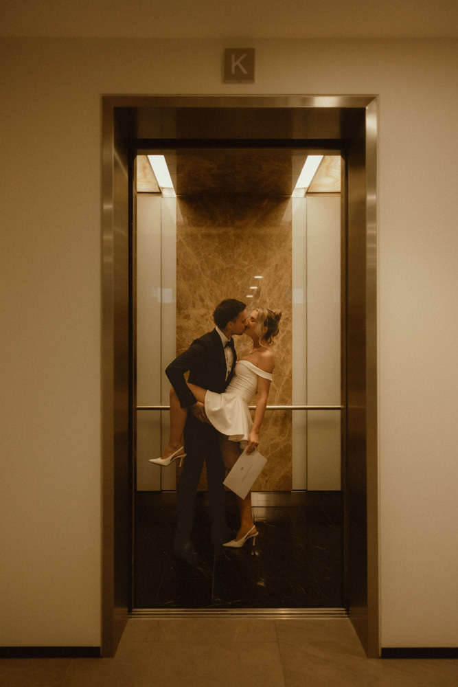 Groom lifting bride for a kiss inside a hotel elevator with marble walls