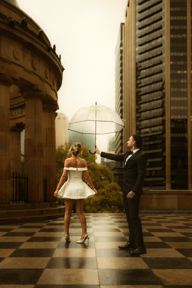 Black and white close-up kiss under a clear umbrella in the rain at Anzac Square