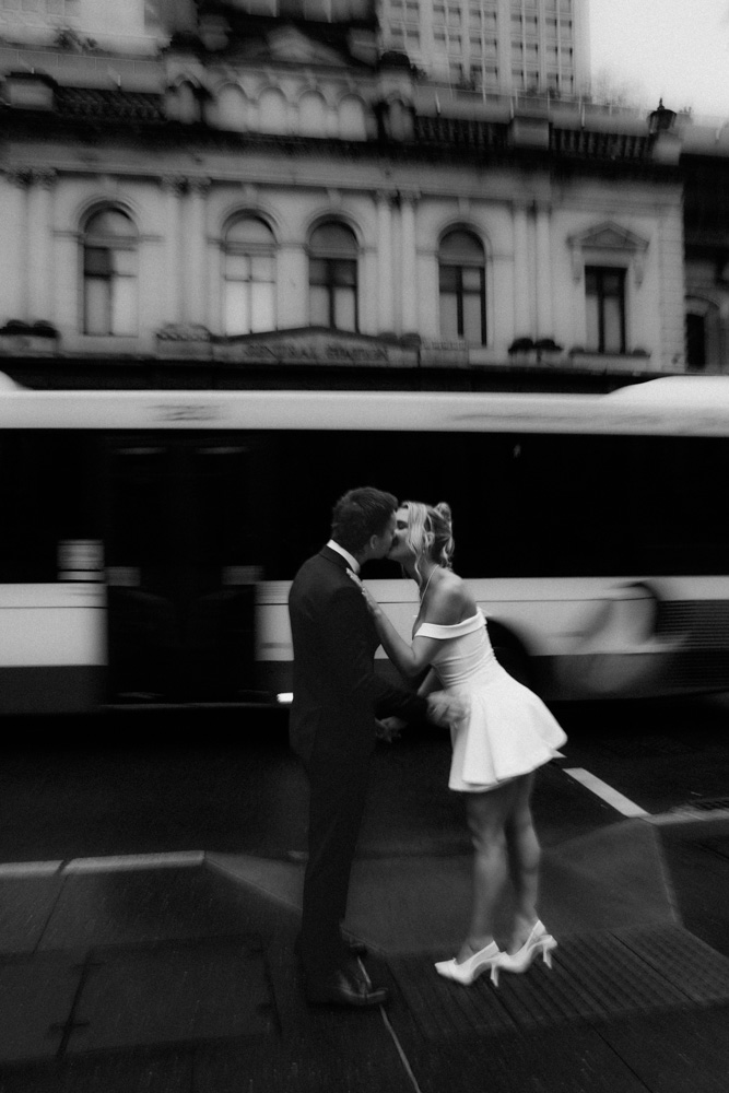 Black and white motion blur of a bus moving behind a newly married couple kissing in Brisbane city for an elopement