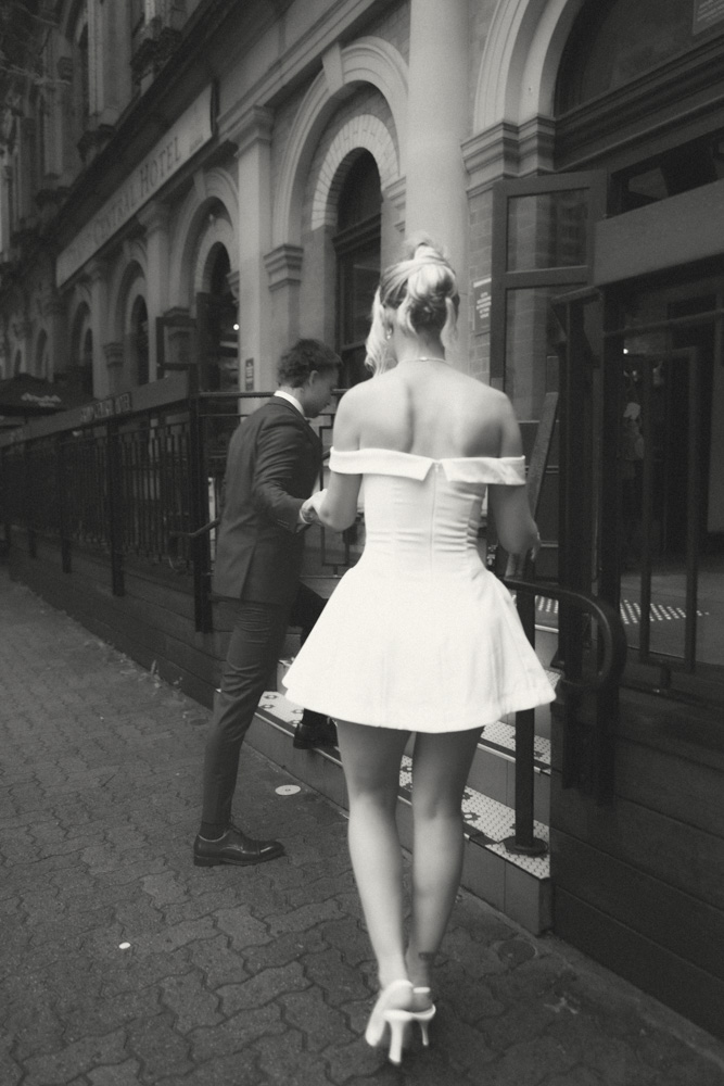 Black and white wide shot of bride and groom running across the street in front of Central Station