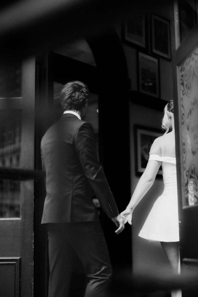Black and white wide shot of bride and groom running across the street in front of Central Station