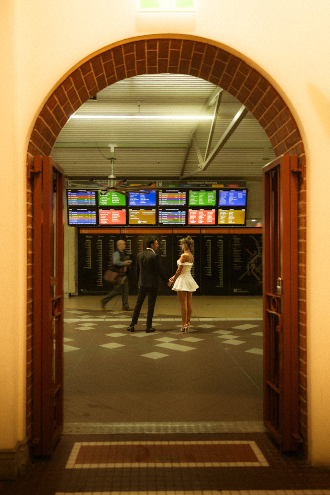 Bride and groom walking through an archway past the station's departure boards, central station Brisbane city