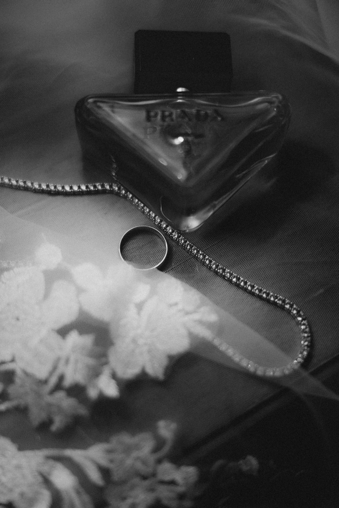 detail black and white image of perfume, rings and necklace