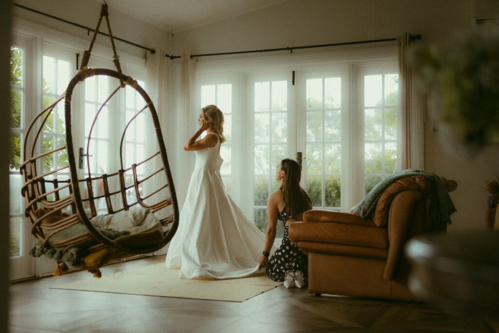 Bridesmaid helping bride into dress in cabin at the lake house fold