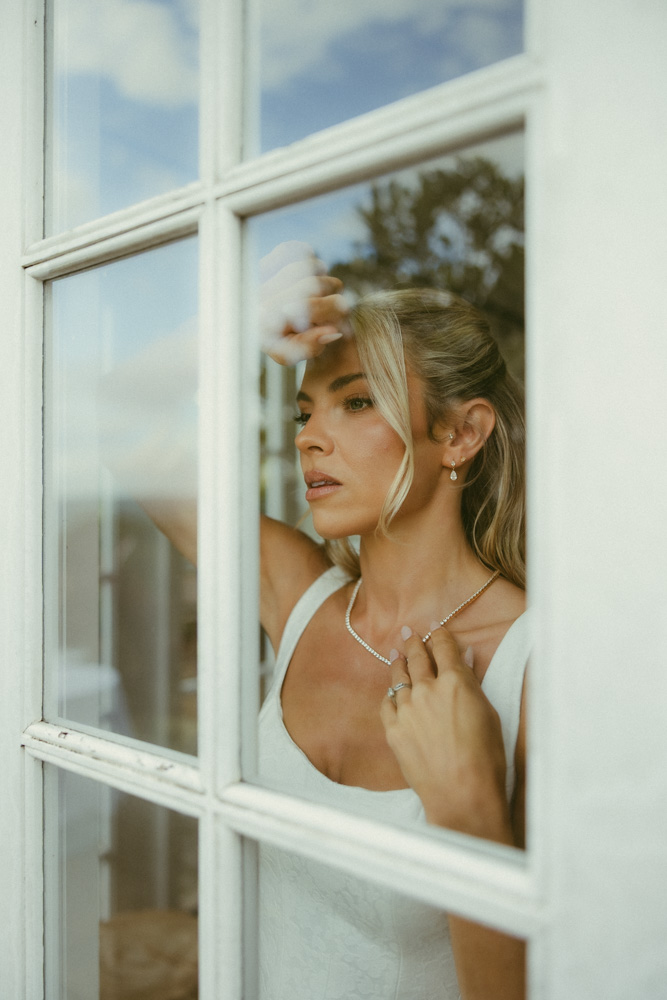 Bride looking out the window wearing wedding dress, touching her necklace in the top cabin 