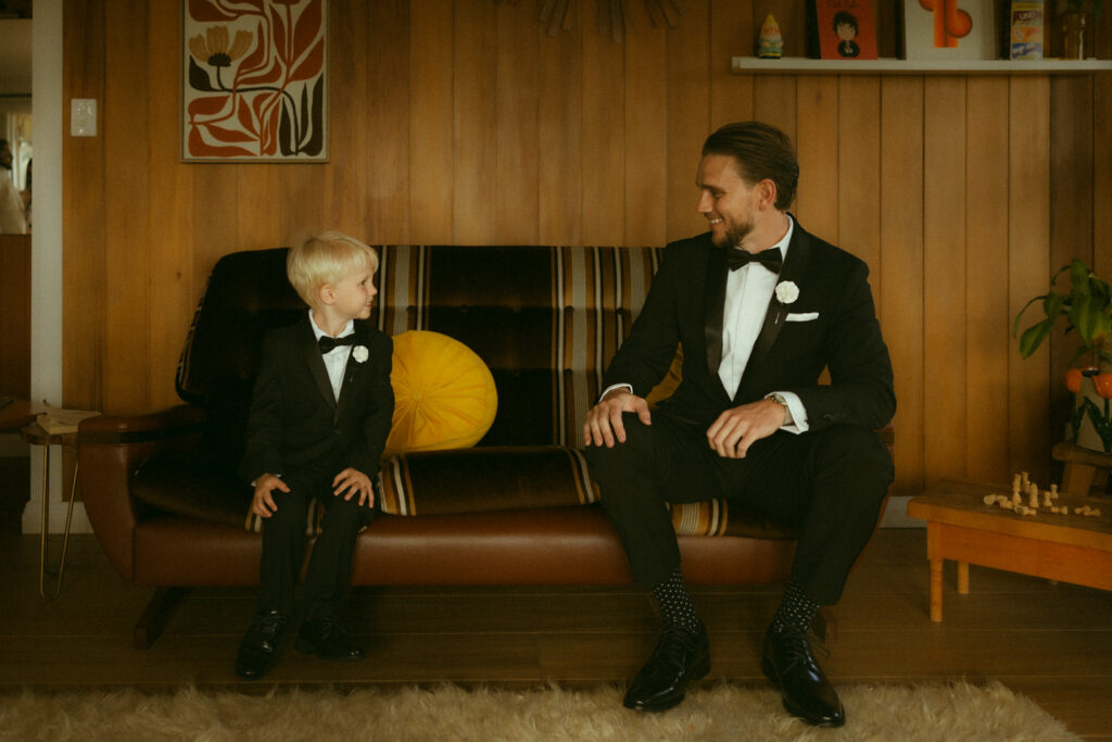 Groom and young son sitting in editorial style pose smiling at each other - getting ready 
