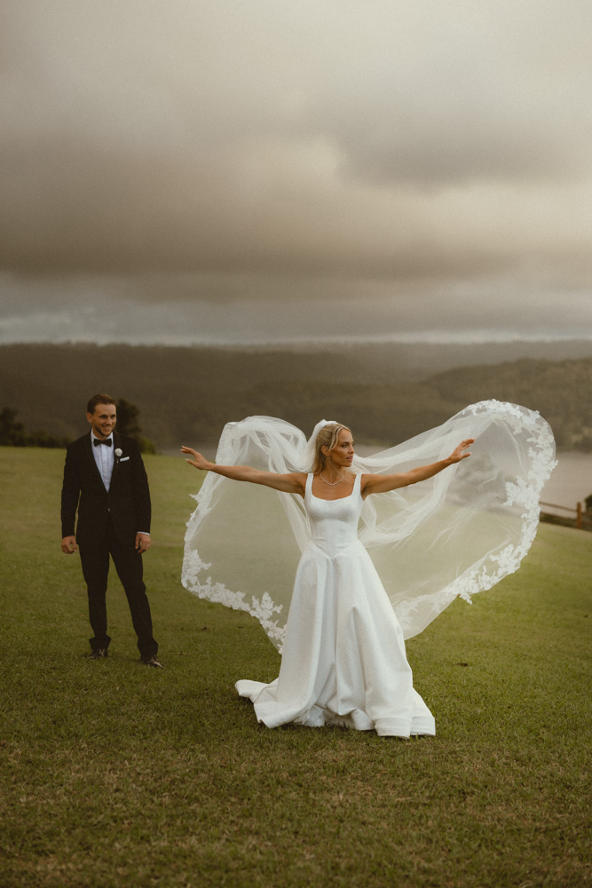Bride throwing veil into air with both arms whilst the groom watches