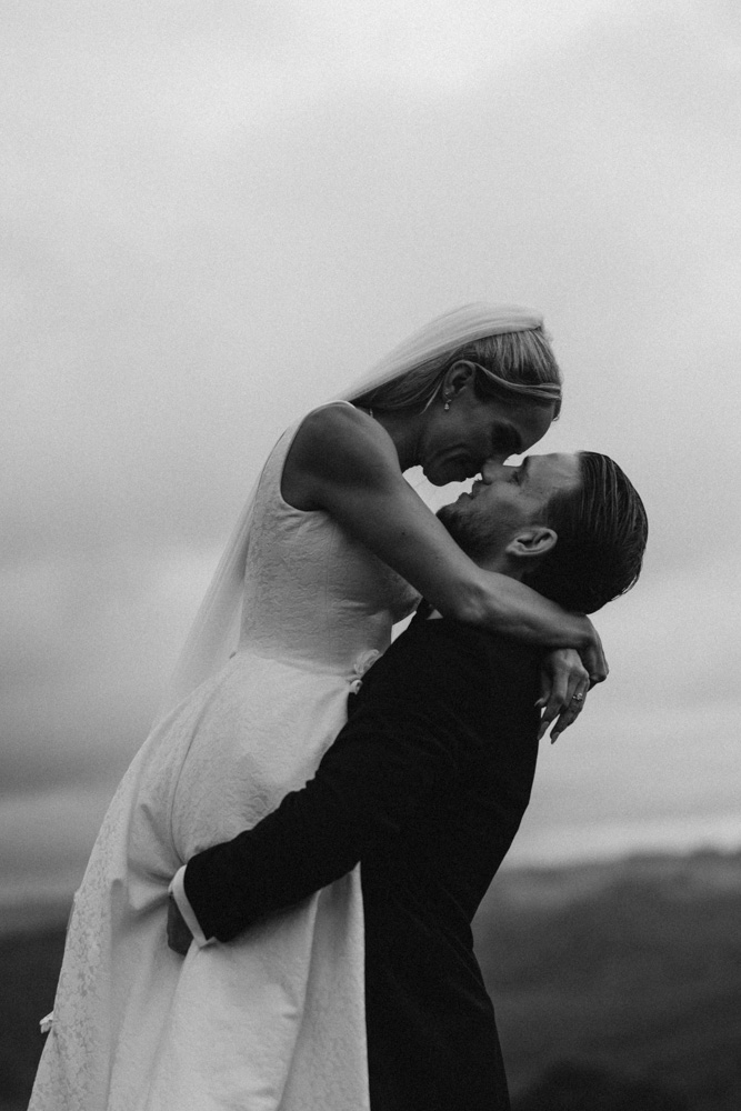 Black and white of groom holding his bride up in the air smiling