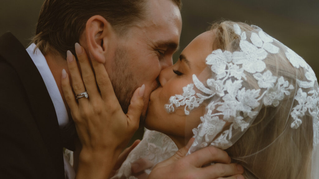 close up of bride wearing a veil and groom kissing 