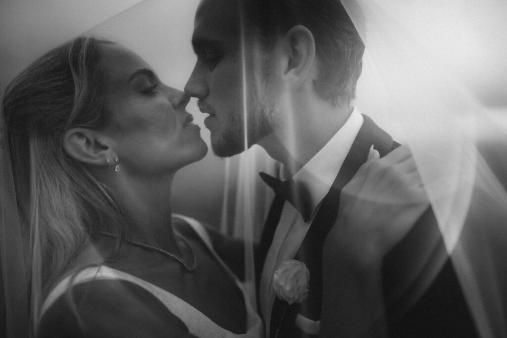 Black and white close up of couple under the veil almost kissing with creative light flairs