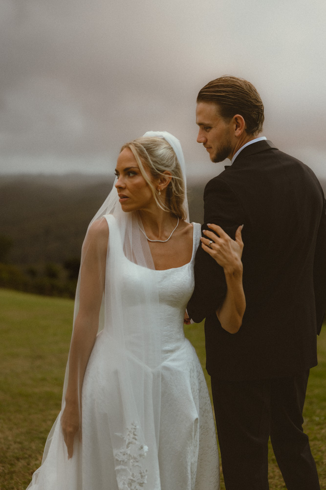 Bride and groom standing on grassy hill wrapped in each others arms 