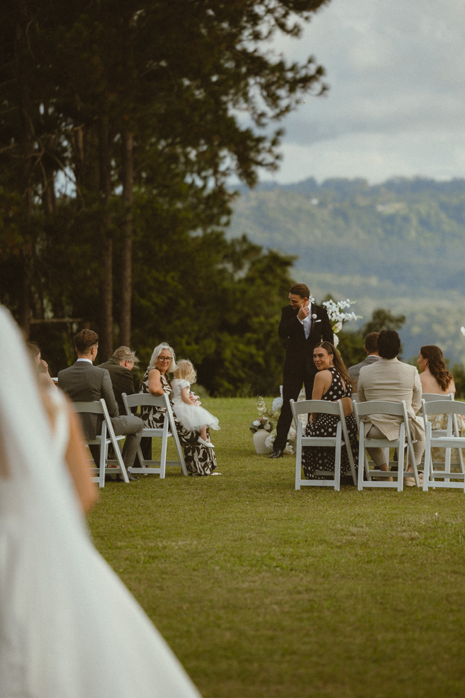 Groom wiping tears away as bride is walking down the isle, while the guests smiling