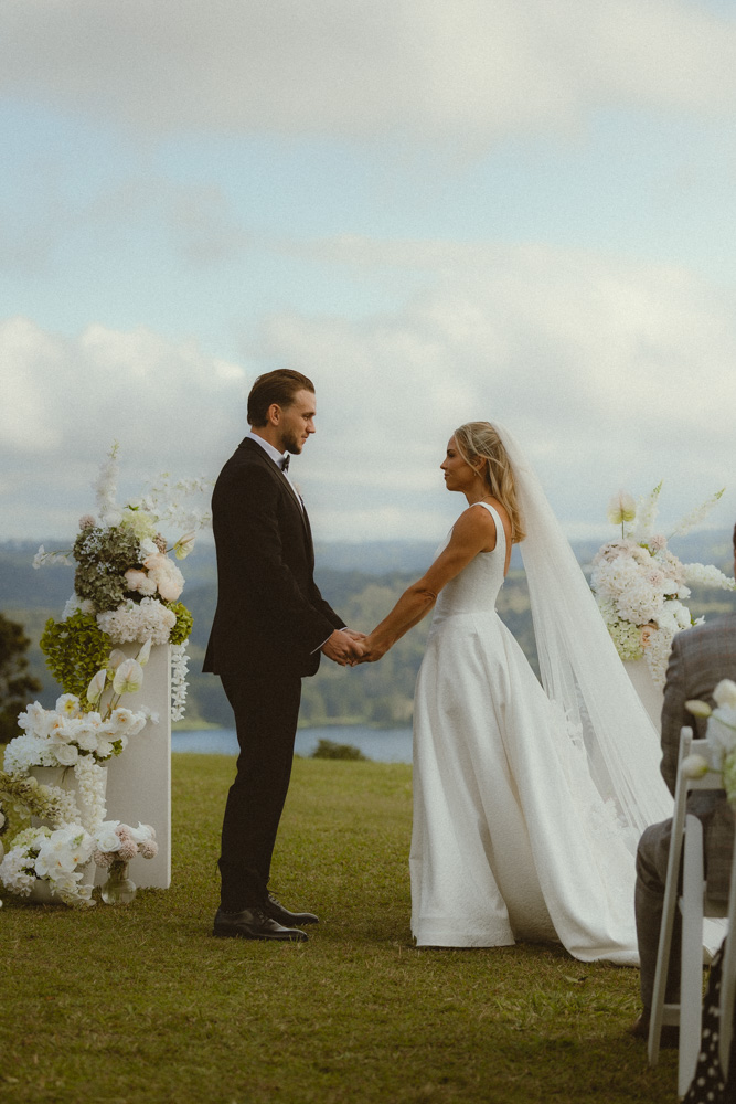 Bride and groom holding hands with lake and sky in the background at their arbour for elopement 