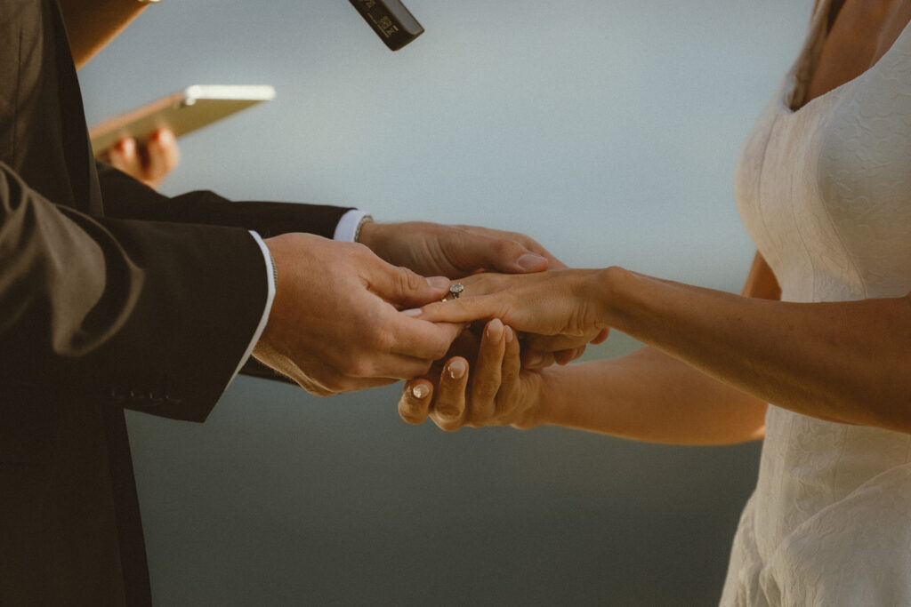 Groom putting ring on brides finger during ring exchange at their ceremony
