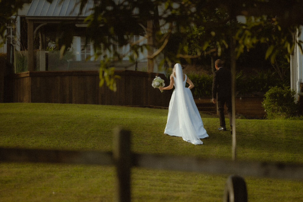 Bride and groom walking up the grass with a fence , having a quiet moment after the ceremony