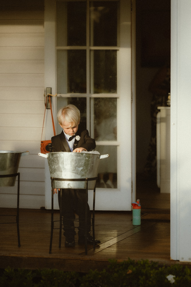 Couples son wearing a tuxedo playing in the champagne ice bucket at The Lake House Folk