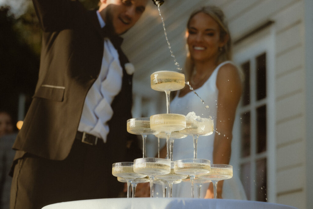 Groom pouring champagne into tower  at golden hour after their elopement